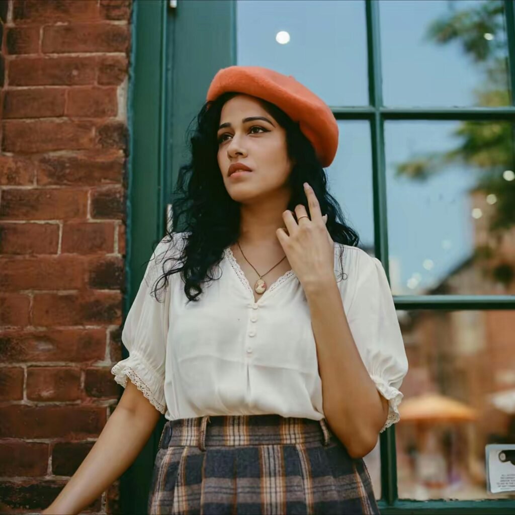 Chic woman with a vintage vibe posing outdoors in a beret and blouse by a window.
